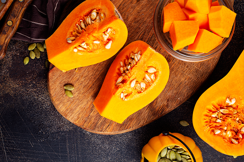 Half cut Pumpkin pieces placed on a wooden plate along with a bowl of pumpkin pieces.
